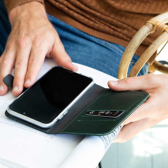 Man met bruine trui opent groene Selencia bookcase met telefoon en creditcard.