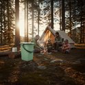 Groene campingtoilet emmer met deksel en rol toiletpapier, naast een tent en kampvuur met gezin.