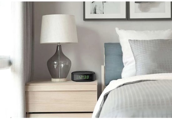 Zwarte Philips wekkerradio op een nachtkastje naast een bed.