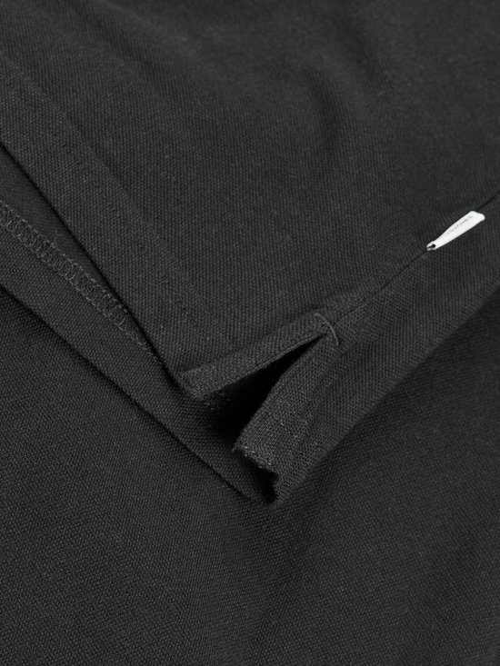 Detail van de split in de zoom van een zwarte poloshirt met korte mouwen.