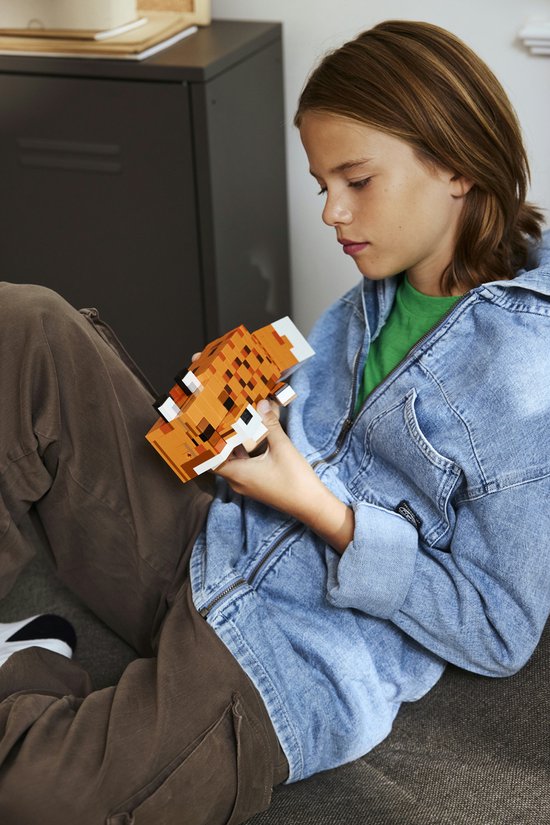 Un garçon avec des lunettes, portant une veste en jean, tient un renard LEGO Minecraft constructible.