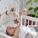 Baby in een ledikantje met een mobiel met gebreide sterren en manen.