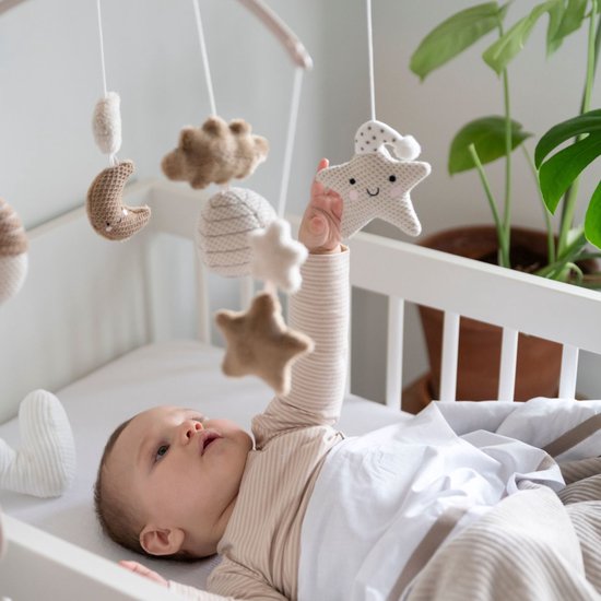 Baby in een ledikantje met een mobiel met gebreide sterren en manen.