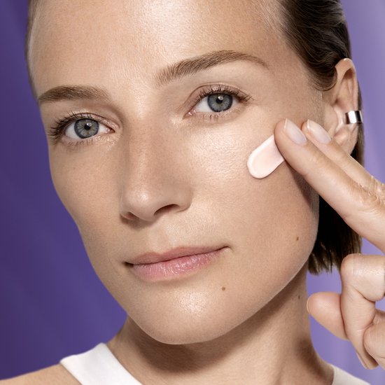 Model brengt een beetje roze Lancôme Rénergie crème aan op haar wang voor een hydraterende verzorging.
