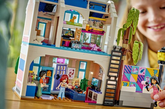 Interieur van LEGO Friends Liann's Familiehuis met speelruimtes en poppetjes, en een meisje dat speelt.