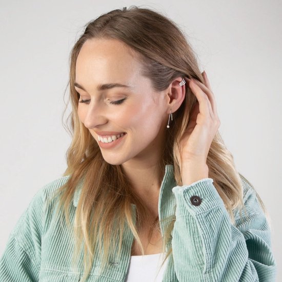 Vrouw met blonde haren, draagt een zilverkleurige oorclip en oorbel.