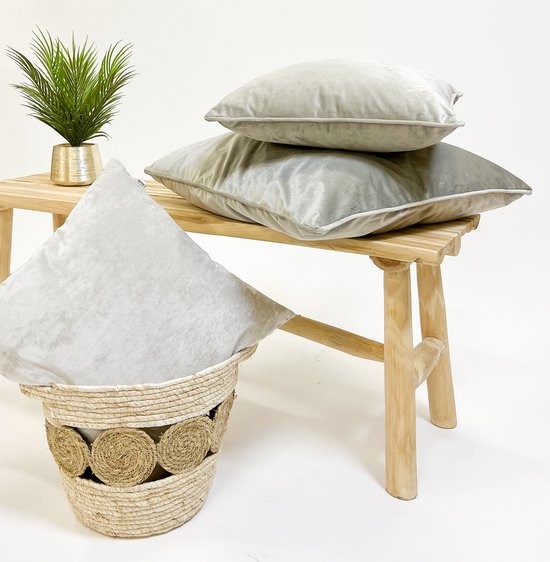 Twee lichtgrijze fluwelen kussens op een houten bankje, naast een rieten mand.