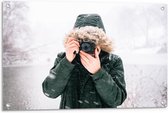 Tuinposter – Man in de Sneeuw met een Donkere Jas met een Bontkraag en een Camera - 90x60cm Foto op Tuinposter  (wanddecoratie voor buiten en binnen)