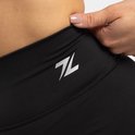 Close-up van een hand die de tailleband van een zwarte sportbroek met ZEUS-logo optrekt.
