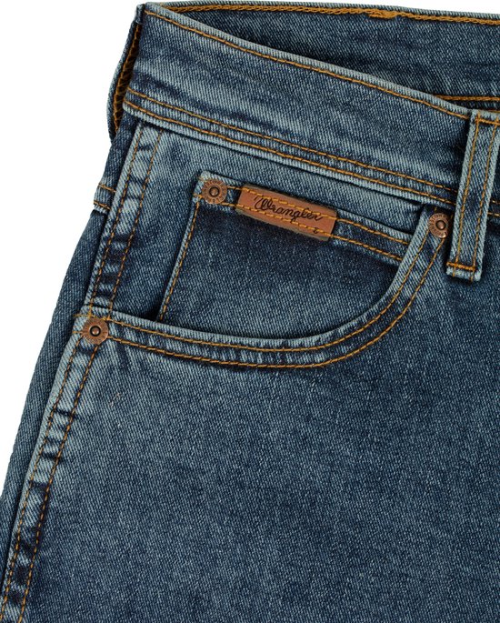 Detail van de zak van een blauwe spijkerbroek met een bruin Wrangler-logo en koperkleurige studs.
