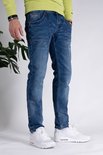 Blauwe spijkerbroek met contrasterende stiksels en een gebruikte wassing. Gedragen door een man met witte sneakers en een limegroene trui.