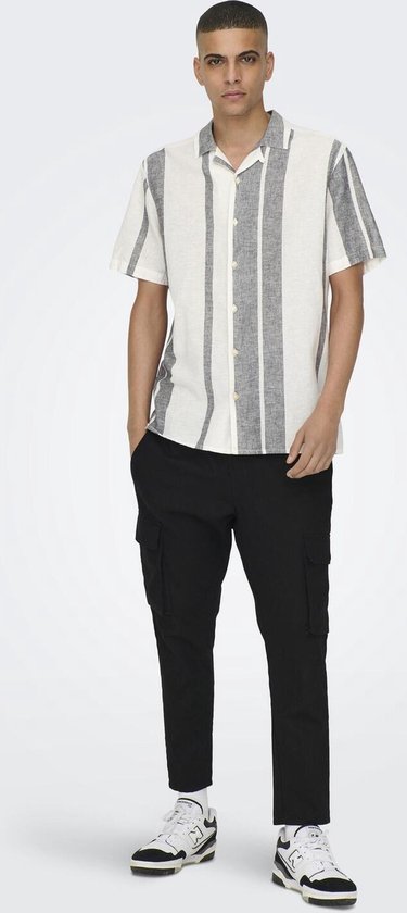 Man in wit kort overhemd met verticale grijze strepen, zwarte broek en sneakers.
