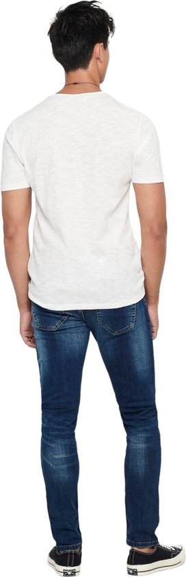 Man in skinny jeans met donkere wassing, wit t-shirt en zwarte sneakers, van achteren gezien.