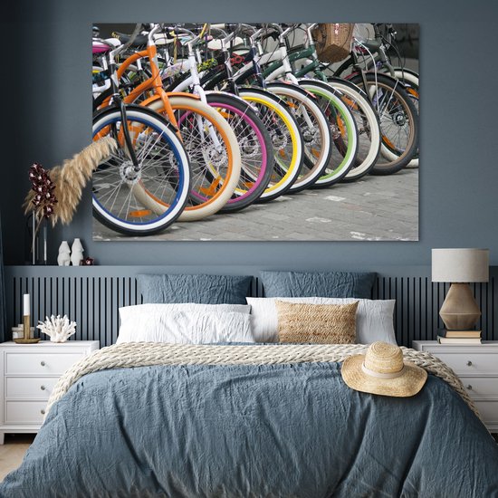 Une rangée de vélos colorés avec des jantes orange, bleues, blanches, roses et jaunes, accrochée au mur d'une chambre.