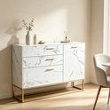 Wit marmerlook dressoir met gouden handvatten en frame, gestyled in een woonkamer met een stoel.
