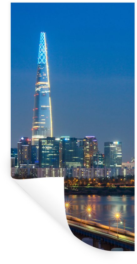 Grote toren van Lotte World in Seoul, verlicht met blauw en geel licht, met een stadsgezicht en een verlichte brug bij nacht.