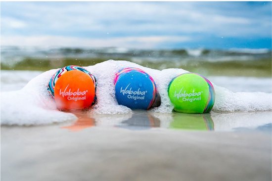 Drie Waboba ballen, oranje, blauw en groen, liggen in het schuim op het strand.