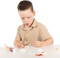 Jongetje met beige shirt schildert met een kwast op een wit gipsen figuur. Diverse andere figuren liggen op tafel.