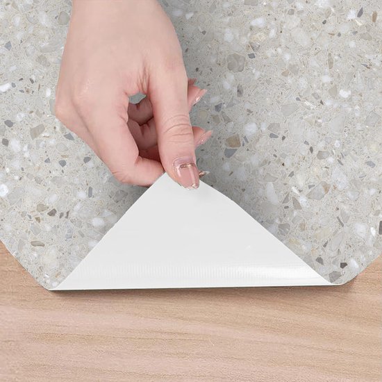 Hand trekt beschermfolie los van lichtgrijze vloerbedekking met terrazzo-print.
