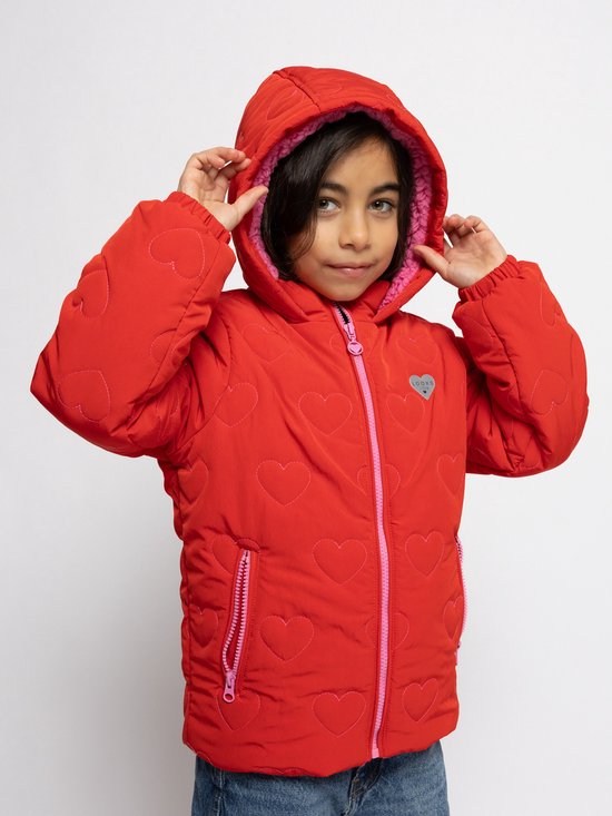 Een meisje met donker haar trekt een rode jas met hartjes en roze voering aan.