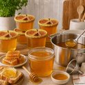Verschillende potten met honing, honingraten, brood met boter en jam, en een pan met honing.