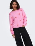 Model in roze trui met all-over rode hartjesprint en zwarte jeans.