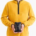 Man in geel fleece met donkergrijze slaapzak in zijn handen, compact opgevouwen.