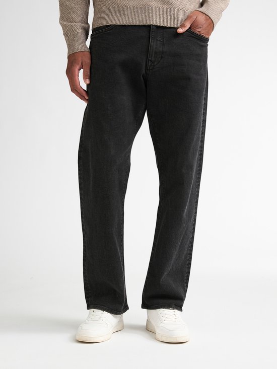 Man in een beige trui en zwarte loose fit jeans, van voren gezien.