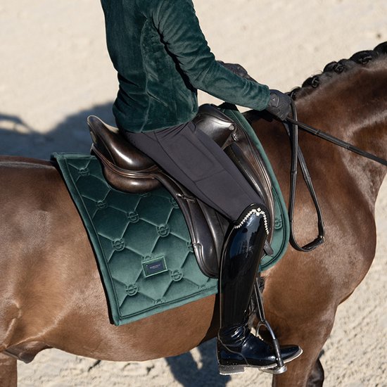 Gedetailleerde opname van een vrouw die op een bruin paard rijdt, met een donkergroen zadeldek.