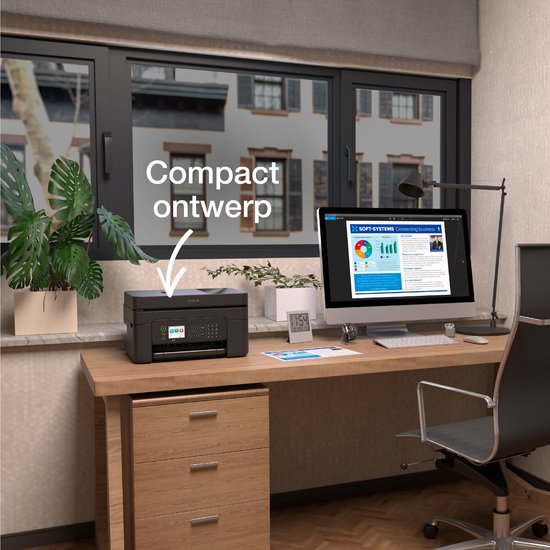 Zwarte Epson WF-2950DWF printer op een houten bureau naast een computer, plant en raam met uitzicht op huizen.