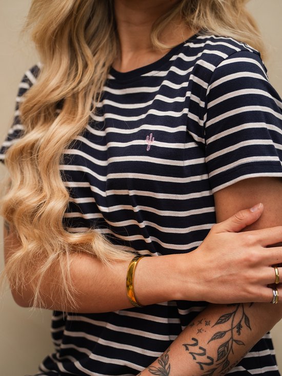 Close-up van een vrouw in een marineblauw en wit gestreept T-shirtjurkje met korte mouwen en een gouden armband.