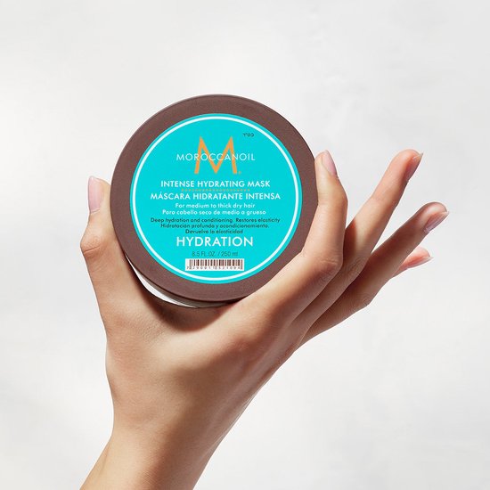 Hand die bruine Moroccanoil pot vasthoudt met turquoise label. "Intense Hydrating Mask" staat op het label.