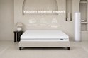 Wit matras met horizontale lijnen op een beige bedframe in een lichte kamer. Tekst en iconen tonen 'Vacuum opgerold verpakt'.