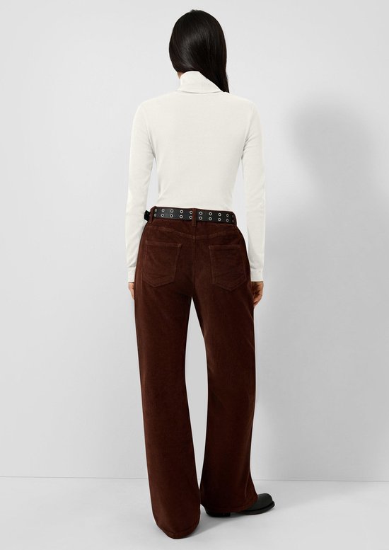 Model van achteren gezien in een witte coltrui en bruine corduroy broek met riem.