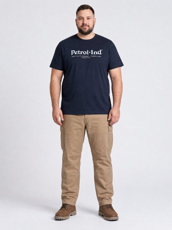 Man met t-shirt met 'Petrol Industries - Steel City Pittsburgh - Pennsylvania 15265 U.S.A.' print, gedragen met cargobroek en bruine schoenen.