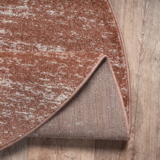 De zoom van een terra oranje rond vloerkleed op een houten vloer, met de achterkant zichtbaar.