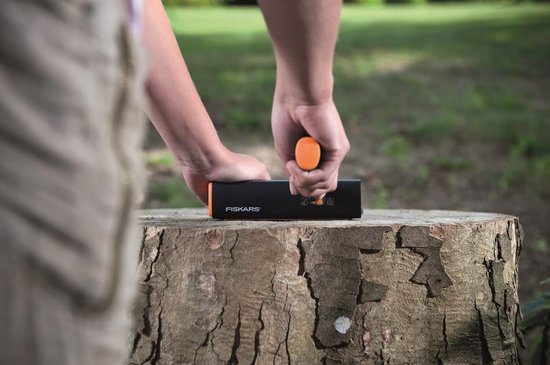 Handen gebruiken de oranje en zwarte Fiskars slijper op een houten stronk.