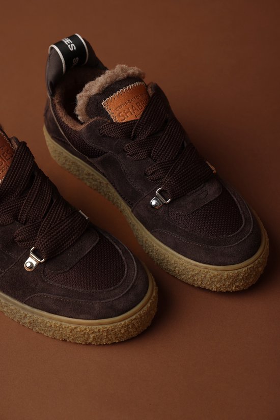 Paar donkerbruine suède sneakers met bontvoering en crèpezool, met logo op de tong.