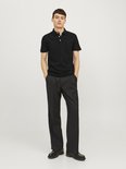 Man in een zwart poloshirt met korte mouwen en zwarte wijde broek.