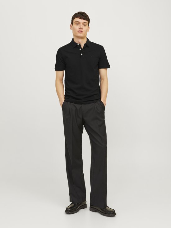 Man in een zwart poloshirt met korte mouwen en zwarte wijde broek.
