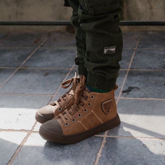 Een kind draagt cognackleurige veterboots met bruine zool en patch.