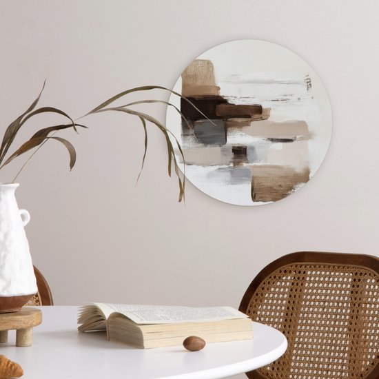 Ronde muurdecoratie met bruine en beige penseelstreken, hangend aan een lichte muur naast een tafel.