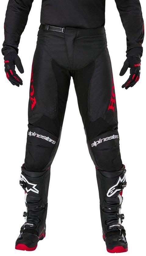 Pantalon de moto noir avec des logos Alpinestars rouges sur les jambes et des genouillères. Porté avec des bottes de moto rouges.