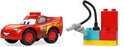 Rode LEGO Duplo Lightning McQueen auto naast een rode, blauwe en gele brandstofpomp met zwarte slang.