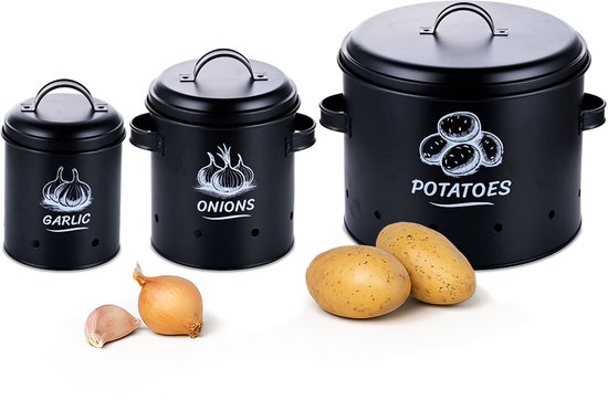 Set van drie zwarte metalen voorraadpotten voor knoflook, uien en aardappelen, met afbeeldingen en tekst. Aardappelen en knoflook liggen ernaast.