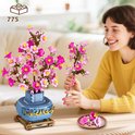 Femme tenant un bouquet de fleurs de cerisier roses dans un vase bleu aux détails dorés.