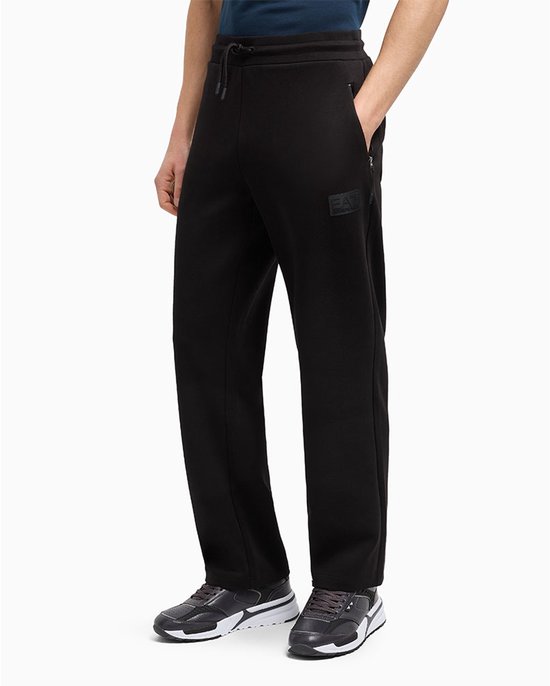 Zwarte trainingsbroek met EA7 logo op linkerbeen en ritssluiting op rechterzak, gedragen door een man.