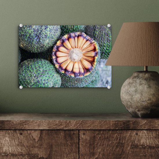 Een glas schilderij van Braziliaans fruit, doorgesneden. Groene schubben aan de buitenkant, oranje en paarse tinten aan de binnenkant.