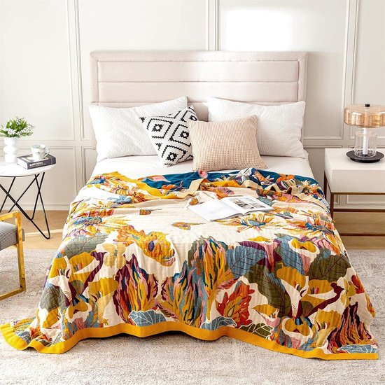 Dubbelzijdige deken met kleurrijke bloemen- en bladprint, op een bed met decoratieve kussens.