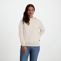 Vrouw met bruin haar, gekleed in een crème hoodie en spijkerbroek, met logo op de heup.